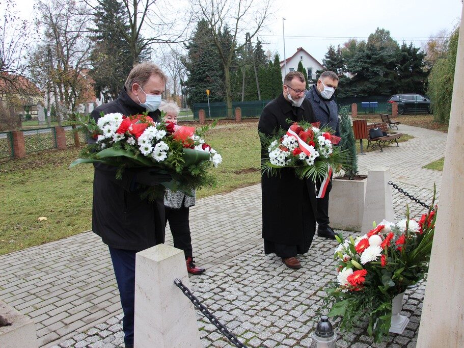 Wójt Tadeusz Kielan, proboszcz Paweł Kajl, sołtys Alina Majewska i przewodniczący Rady Gminy Norbert Grabowski składają kwiaty pod tablicą pamięci Józefa Piłsudskiego.