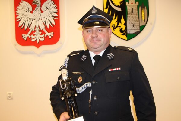 Łukasz Kurek trzyma statuetkę strażaka roku.